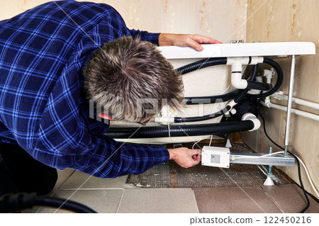 Plumber installing electrical box for jetted bathtub, he adjusting plumbing and electrical connections. Plumber installing electrical box for jetted bathtub, he adjusting plumbing and electrical connections. 122450216