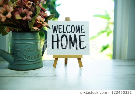 Welcome Home quotes text on paper card with easel and flowers in metal vase in the window background 122450321