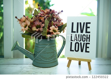 Live Laugh Love quotes text on paper card with easel and alarm clock in the window background 122450322