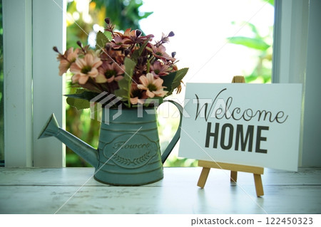 Welcome quotes text on paper card with easel and flowers in metal vase in the window background 122450323