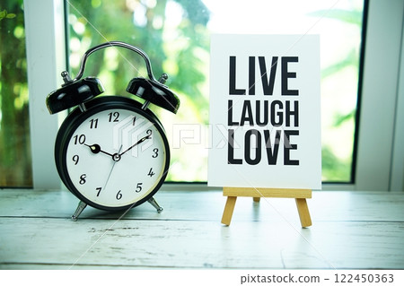 Live Laugh Love paper card with easel and alarm clock in the window background Live Laugh Love paper card with easel and alarm clock in the window background 122450363