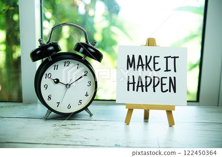 Make It Happen quotes text on paper card with easel and alarm clock in the window background 122450364