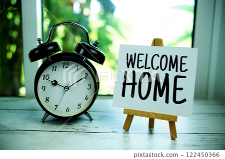 Welcome Home quotes text on paper card with easel and alarm clock in the window background 122450366