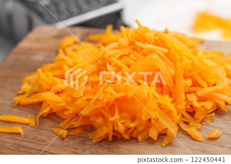 Shredded pumpkin on wooden cutting board. Metal grater in blur. Cooking preparation and vegan vegetable meal concept Shredded pumpkin on wooden cutting board. Metal grater in blur. Cooking preparation and vegan vegetable meal concept 122450441