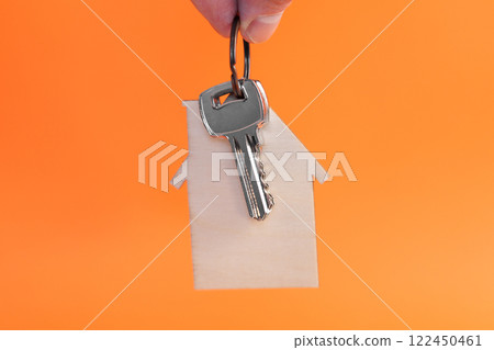 Hand holding a apartment keys on wooden house shaped keyring. Creative orange color background 122450461