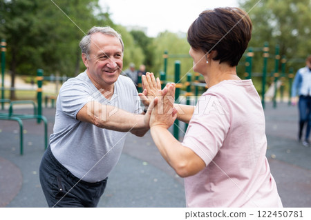 Elderly man and woman doing gymnastics on outdoor sports ground Elderly man and woman doing gymnastics on outdoor sports ground 122450781