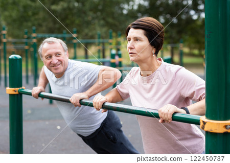 Elderly couple doing push-ups on crossbar together on sports ground of city park 122450787