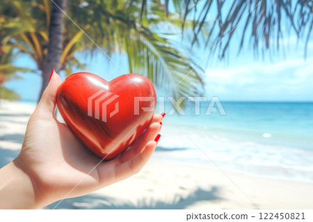 Wooden heart held by a woman hands with red nails on sunny tropical beach with palm leaves in the background. Close-up. Summer love concept 122450821
