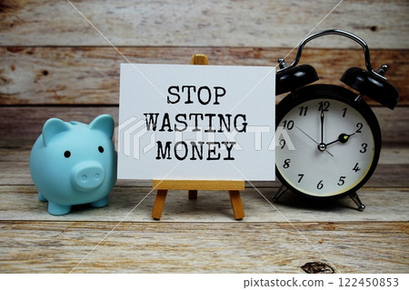 Stop Wasting Money text on paper card with alarm clock and piggy saving on wooden baciground, Money saving concept 122450853