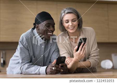 Friendly middle aged multiethnic couple share information between two smartphones Friendly middle aged multiethnic couple share information between two smartphones 122451053