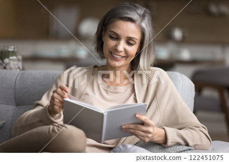 Smiling 50s female spend evening at home read book Smiling 50s female spend evening at home read book 122451075