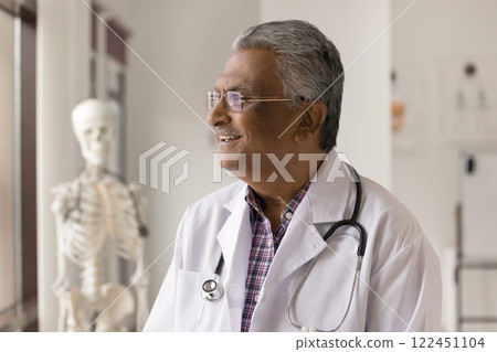 Happy old male doctor looking at window at clinic office 122451104