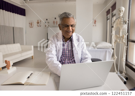 Smiling mature Indian doctor use notebook at modern work office Smiling mature Indian doctor use notebook at modern work office 122451157
