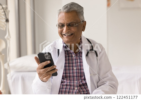 Smiling mature doctor read message from grateful patient on phone 122451177