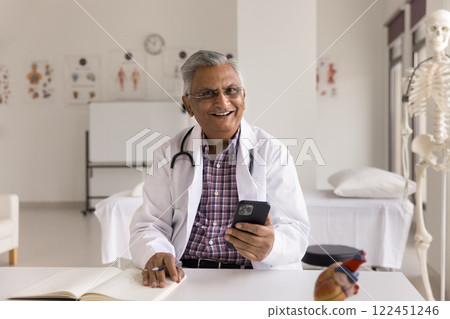 Portrait smiling senior man doctor sit at desk hold smartphone 122451246