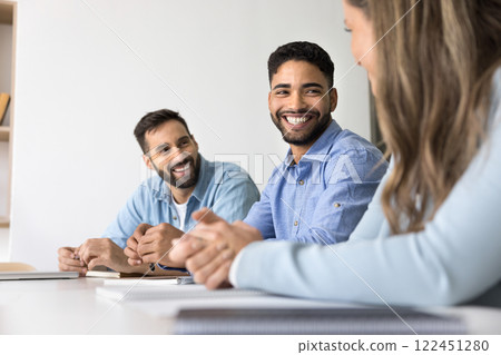 Multinational laughing teammates sit at table in conference room Multinational laughing teammates sit at table in conference room 122451280