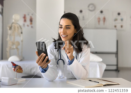 Happy woman doctor use telehealth app on phone at workplace Happy woman doctor use telehealth app on phone at workplace 122451359