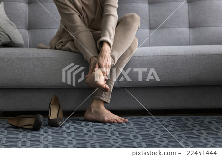 Middle aged woman sit on couch barefoot massaging fatigue feet 122451444