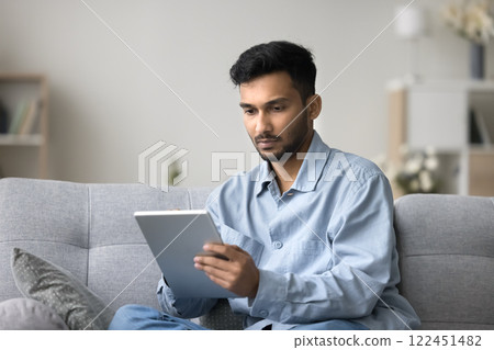 Focused young male freelancer working from home using digital tablet Focused young male freelancer working from home using digital tablet 122451482