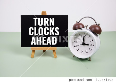 Turn Clocks Ahead text on paper card with alarm clock on green background Turn Clocks Ahead text on paper card with alarm clock on green background 122451498