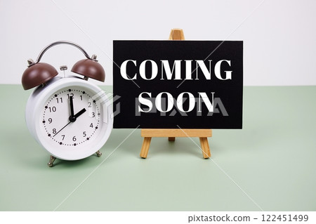 Coming soon text on paper card with alarm clock on green background 122451499