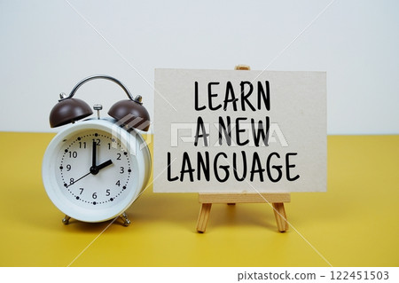 Learn A New Language text on paper card with alarm clock on yellow background 122451503