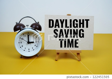 Daylight saving time text on paper card with alarm clock on yellow background 122451505