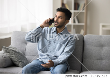 Confident young male sitting on sofa speak on mobile telephone Confident young male sitting on sofa speak on mobile telephone 122451514