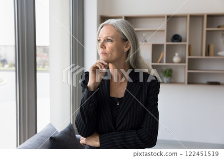 Professional 50s businesswoman looking out window with pensive, thoughtful expression Professional 50s businesswoman looking out window with pensive, thoughtful expression 122451519