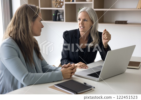 Female workmates lead conversation seated at workplace table with laptop 122451523