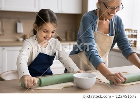 Preteen girl in apron imitate granny rolling dough with pin 122451572