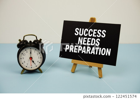 Success Needs Preparation text on paper card with alarm clock on blue background Success Needs Preparation text on paper card with alarm clock on blue background 122451574