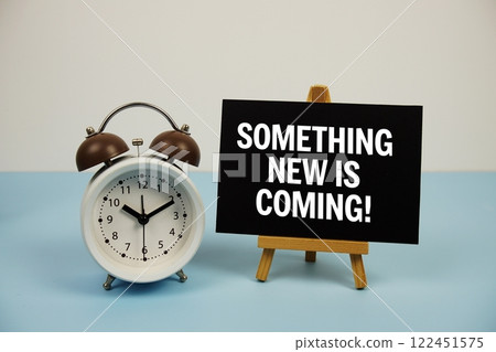 Something new is coming text on paper card with alarm clock on blue background Something new is coming text on paper card with alarm clock on blue background 122451575