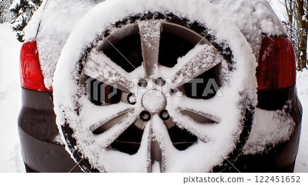 Snow covering spare wheel mounted on back of car in winter 122451652