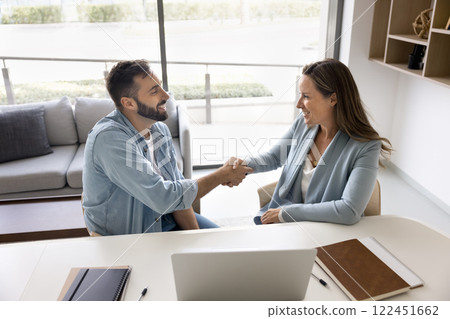 Two multiethnic businesspeople shaking hands after negotiations in office Two multiethnic businesspeople shaking hands after negotiations in office 122451662