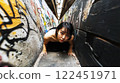 Young woman crawling in narrow graffitied alleyway 122451971