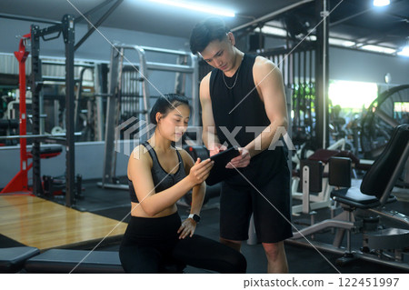 Fitness coach reviewing a training plan on digital tablet with female client in the gym 122451997