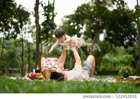 Father lifting his adorable son into the air during a picnic in the park 122452018
