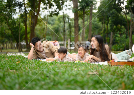 Happy family having a picnic on a beautiful day in green park. Parenting, family, and outdoor leisure concept 122452019