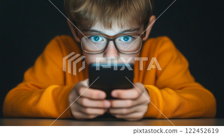 A boy, stressed, stares blankly at a smartphone, its light reflecting in their glasses, internet addiction concept A boy, stressed, stares blankly at a smartphone, its light reflecting in their glasses, internet addiction concept 122452619