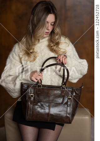 A girl in a warm sweater, a black short skirt, nylon tights is posing with a brown leather bag. A girl in a warm sweater, a black short skirt, nylon tights is posing with a brown leather bag. 122452728