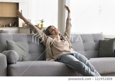 Mature woman stretch arms sitting on couch with closed eyes 122452809