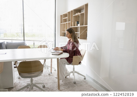 Businesswoman typing on laptop seated at desk in conference room 122452819