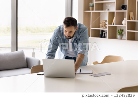 Focused businessman leaning at desk working on laptop 122452829