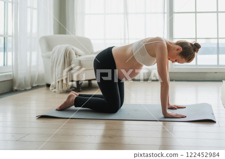 Pregnancy yoga fitness workout training. Pregnant woman practicing yoga at home. Pregnant girl doing sports exercise on yoga mat indoor. Woman with big belly have fitness training practicing asana 122452984