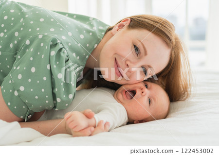 Happy family at home. Mother playing with little toddler child on bed. Mom baby relax playing having fun together. Mother looks at camera with love care. Mom of breast feeding baby rest in living room Happy family at home. Mother playing with little toddler child on bed. Mom baby relax playing having fun together. Mother looks at camera with love care. Mom of breast feeding baby rest in living room 122453002
