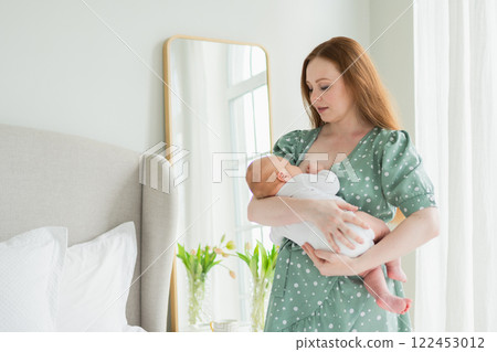 Happy family at home. Mother breastfeeding baby for health nutrition wellness. Mom nursing feeding her newborn child milk at home. Woman infant girl in white bedroom Mother hugs baby with love care Happy family at home. Mother breastfeeding baby for health nutrition wellness. Mom nursing feeding her newborn child milk at home. Woman infant girl in white bedroom Mother hugs baby with love care 122453012