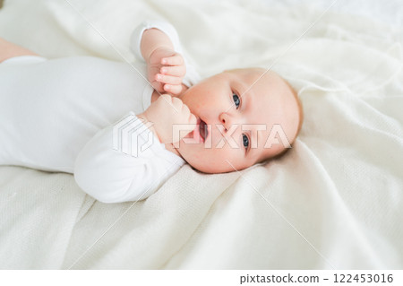Happy baby. Cute little newborn girl with smiling face lying on bed in bedroom. Infant baby resting playing lying down on white blanket at home. Motherhood happy child childcare concept 122453016