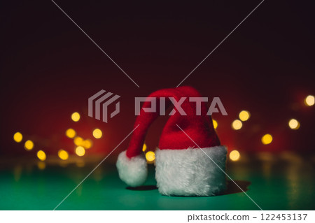 Santa hat on isometric green red background. Defocused lights on backdrop Copy space for your text. Mock up for advertisement. Holiday Christmas composition. Minimalistic greeting card Santa hat on isometric green red background. Defocused lights on backdrop Copy space for your text. Mock up for advertisement. Holiday Christmas composition. Minimalistic greeting card 122453137