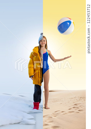 Girl dressed in yellow winter jacket on one side, and blue swimsuit on another. One foot in snow, one in sand, with beach ball in hand. 122453712